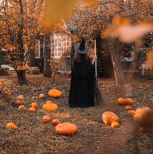 Girl in witch costume in yard with pumpkins